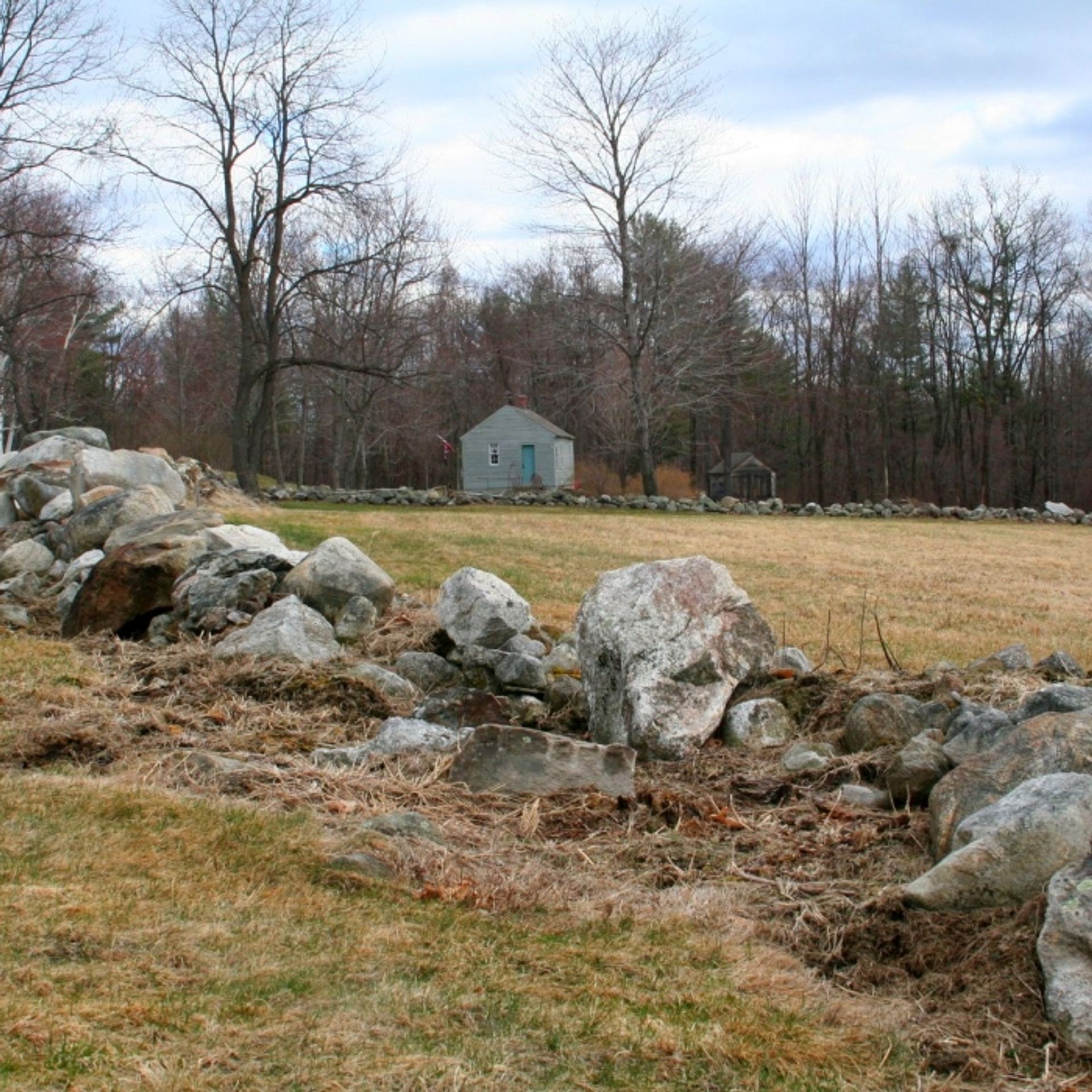 A stone wall with a view of the historic house at Monson Center behind.