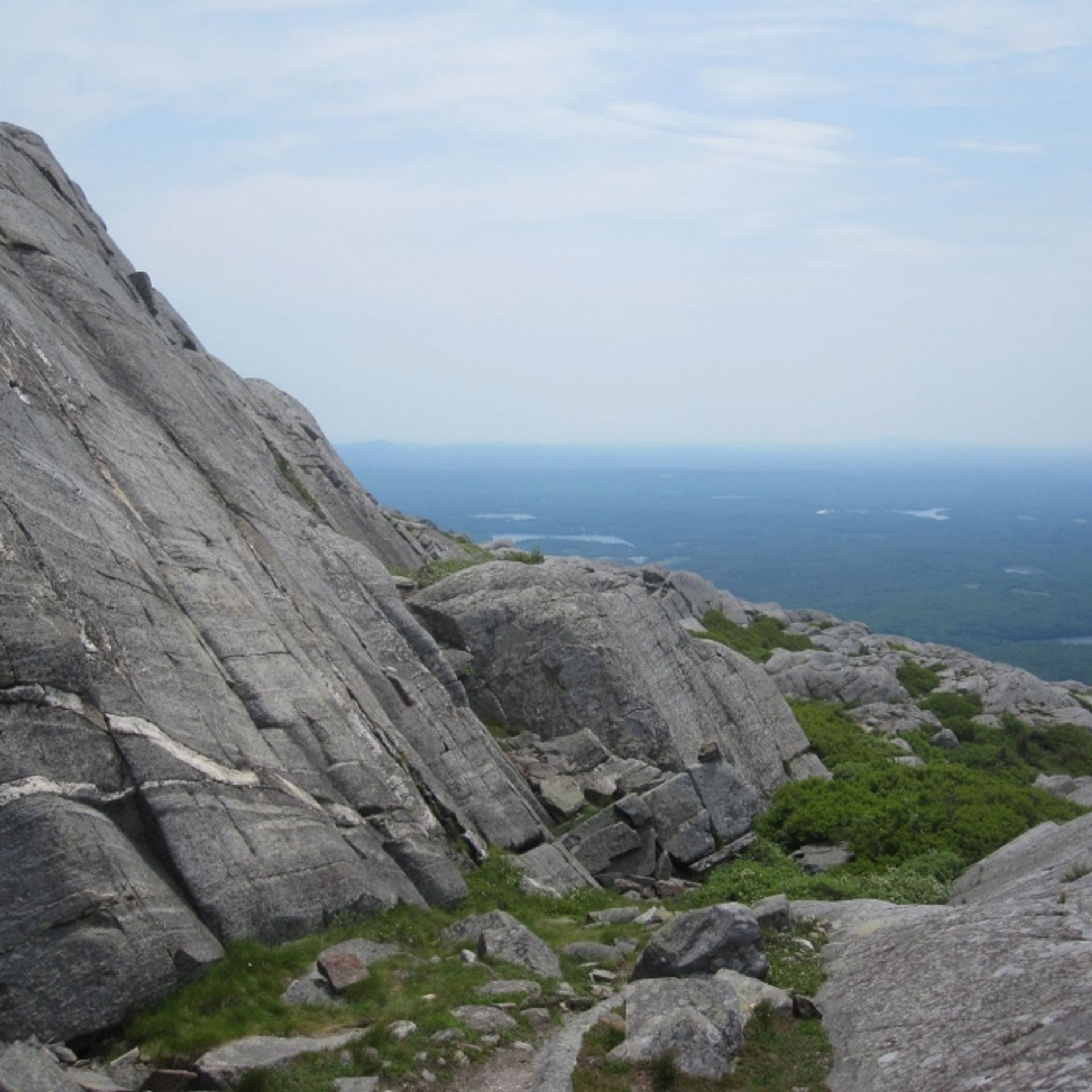 Steep granite cliffs with a view of lakes and forest beyond.