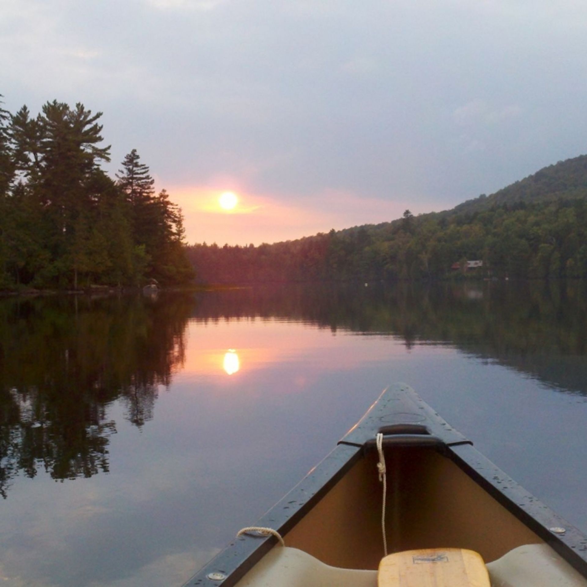 A sunset view reflected on the water, taken from a canoe.