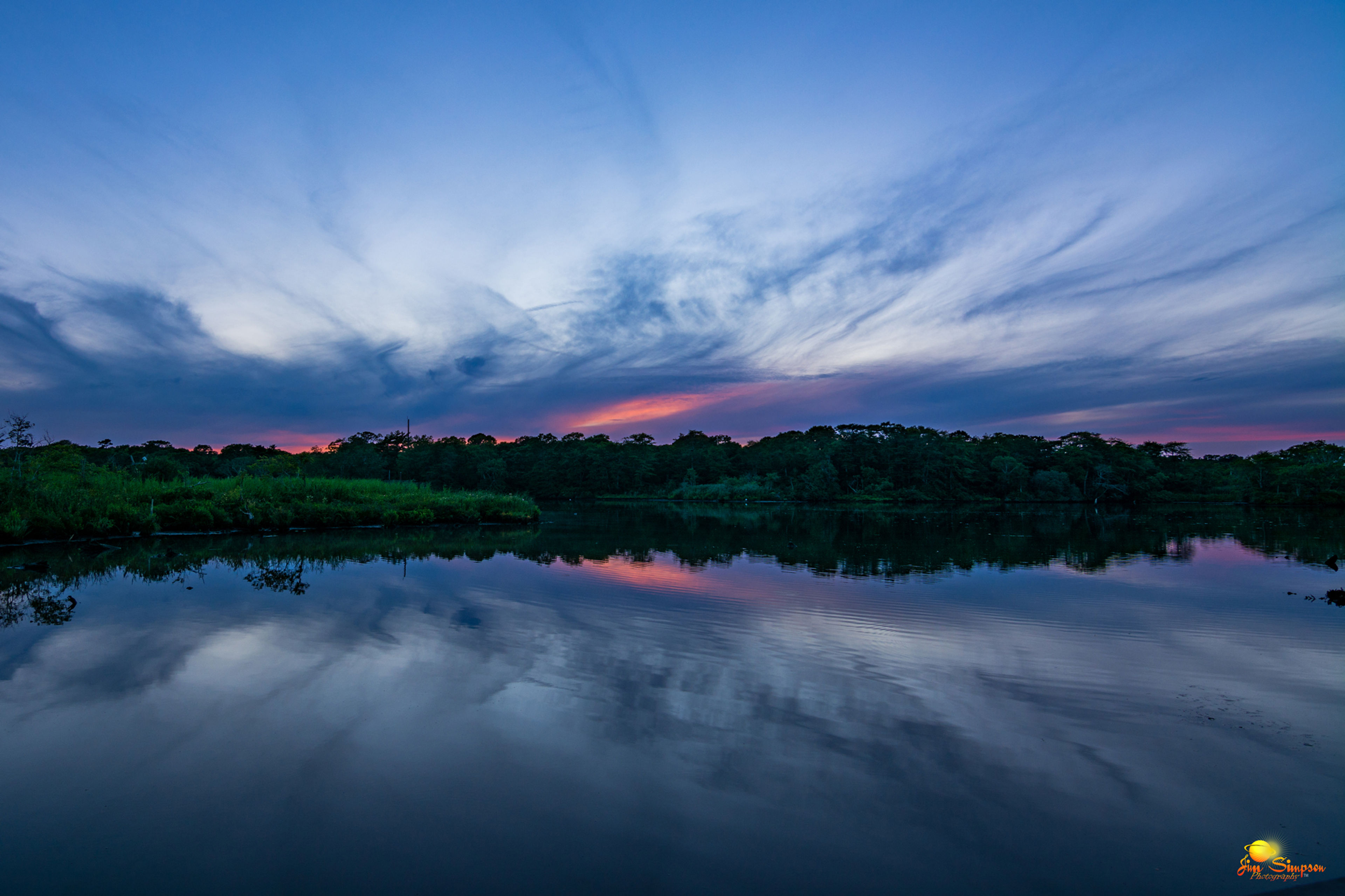 The sunset along the Carmans River lights up the summer sky with brilliant shades of pink and blue separated by the deep green of the riparian forest edges.