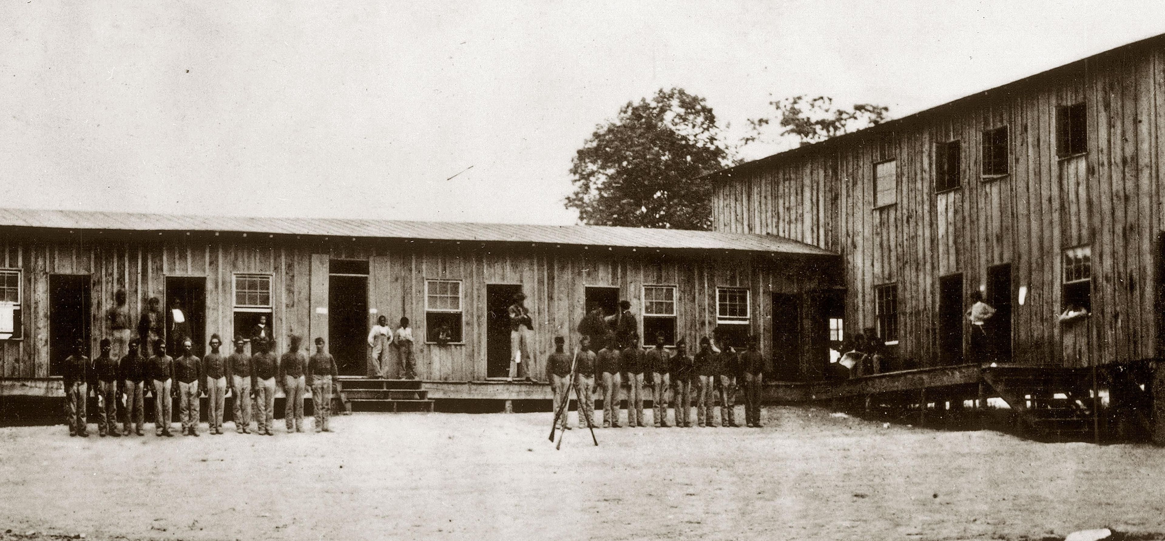 African American Civil War soldiers fighting for the Union stand at attention outside their barracks at Camp Nelson, KY.