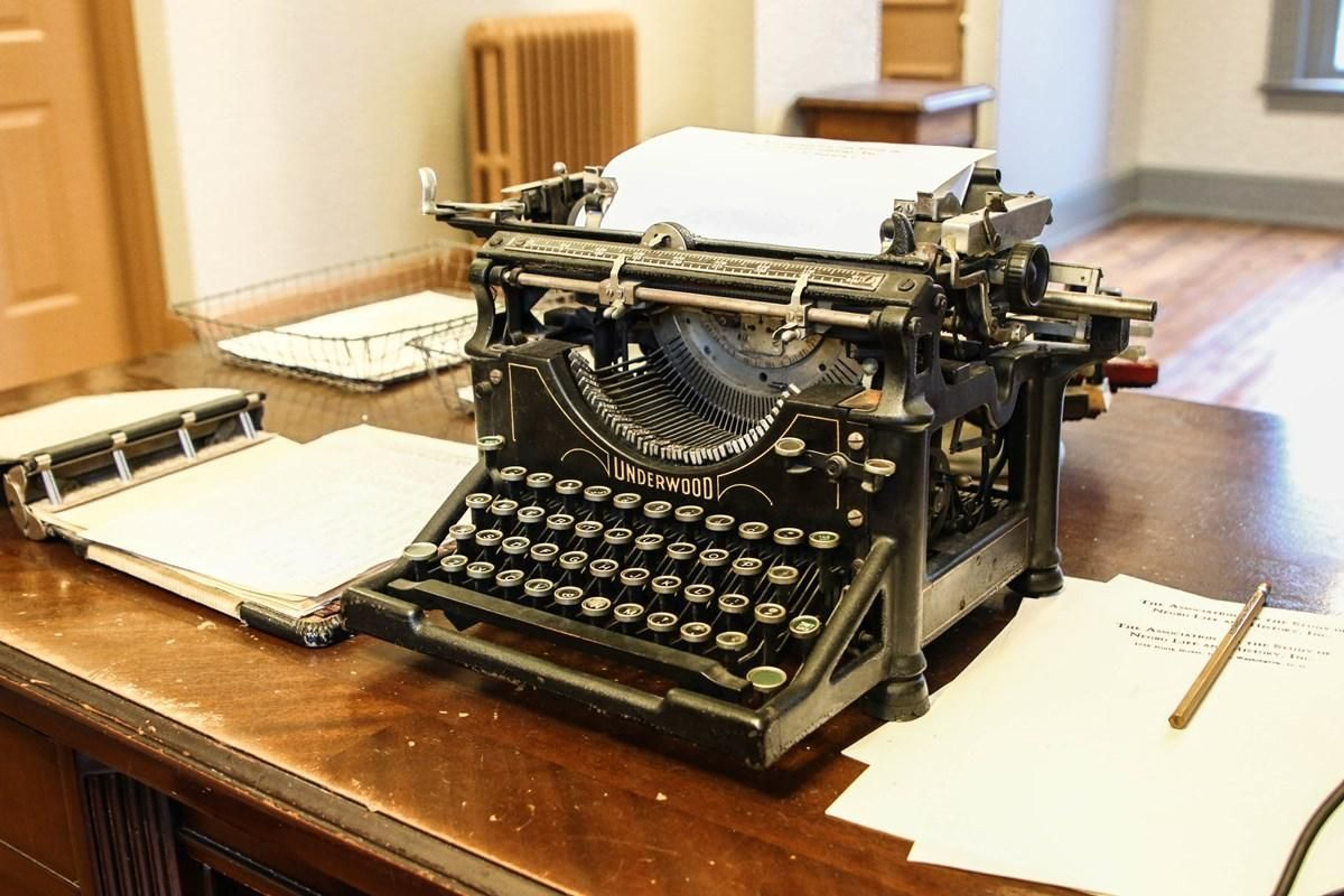 An old-fashioned typewriter sits on top of a desk along with other office supplies in the reception area and office space of Dr. Woodson's office-home.