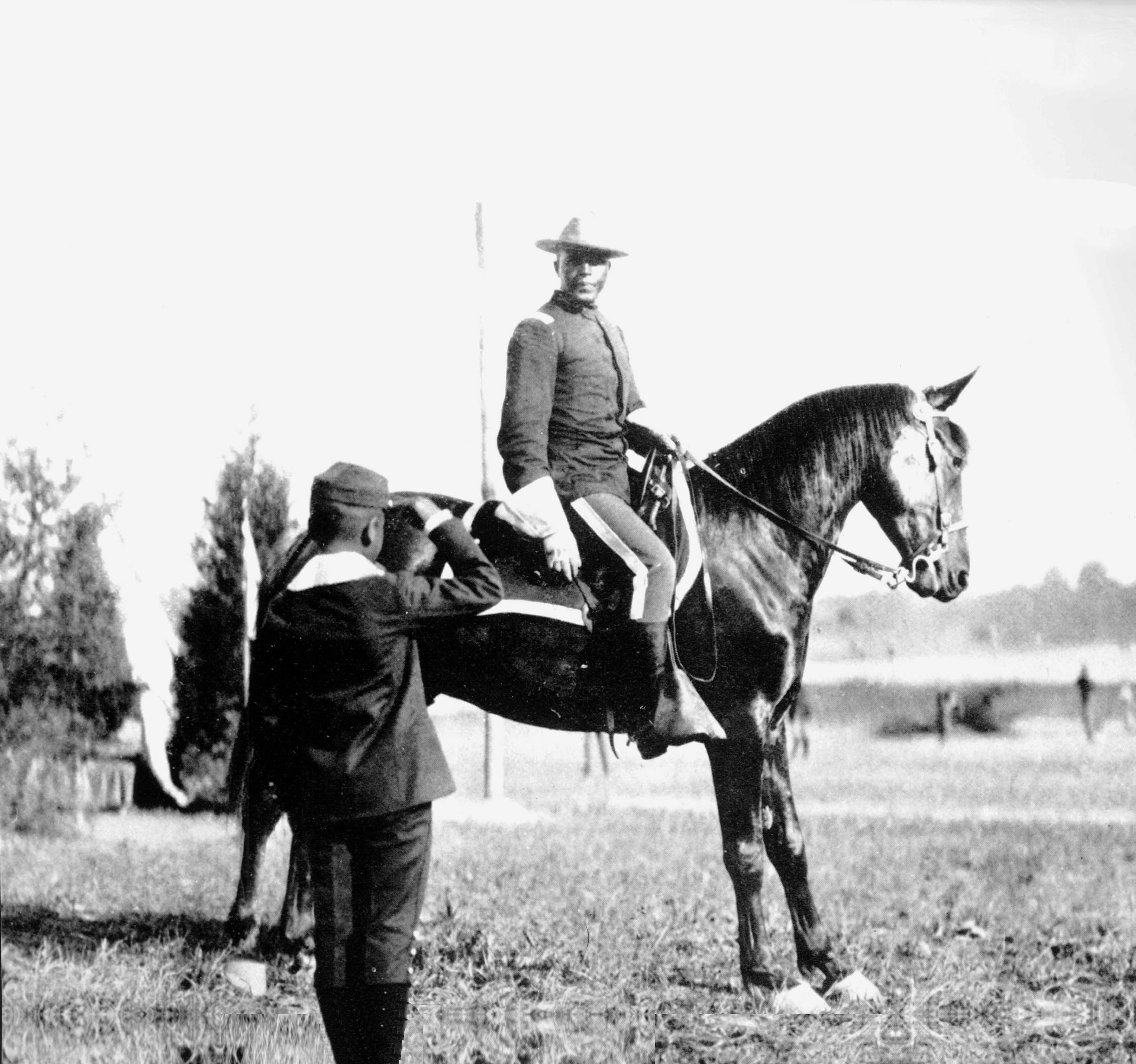 Charles Young poses for a portrait with one of his horses as he is saluted by a young, unidentified boy.