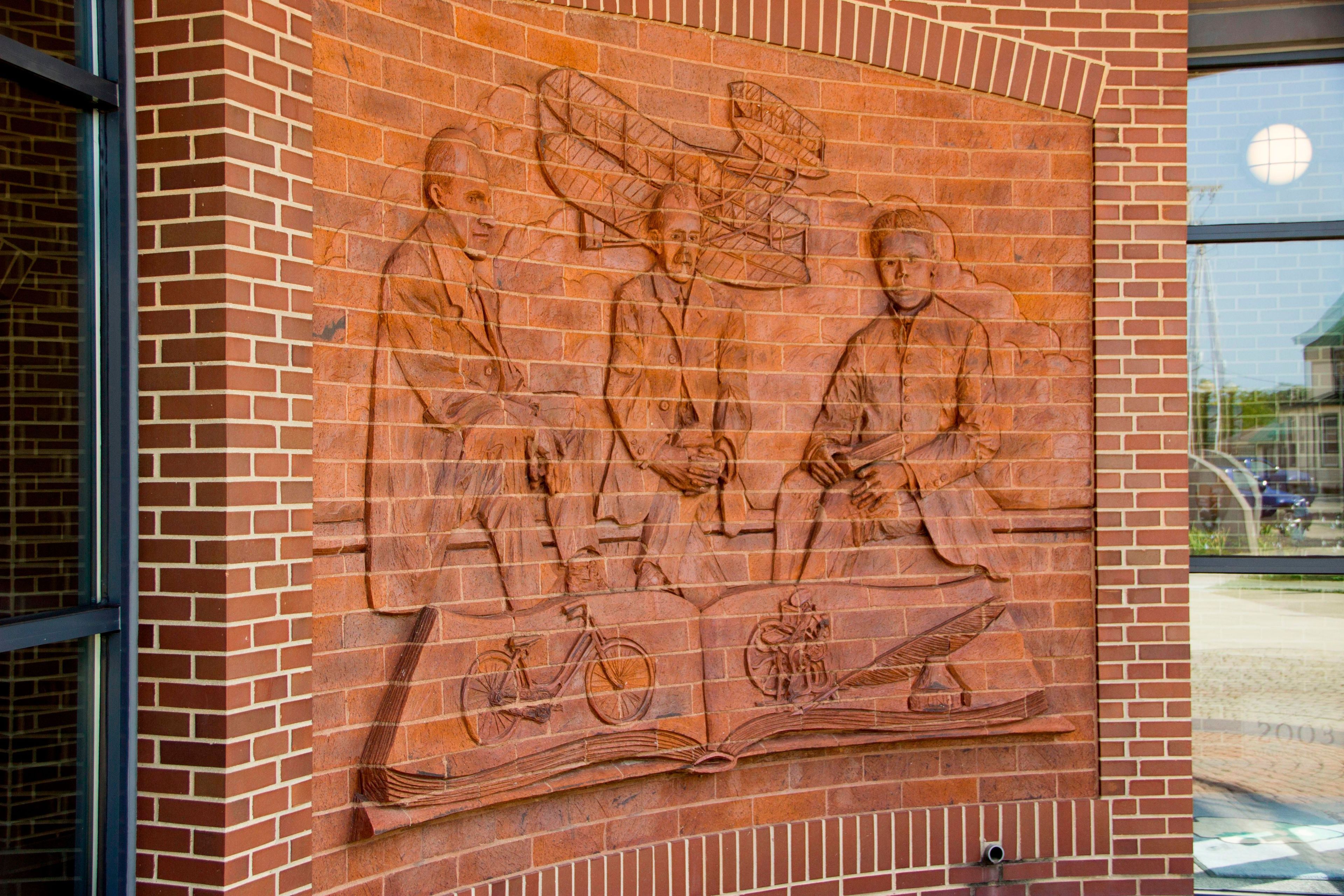 An artistic mural etched out of the red brick wall at the Wright-Dunbar Interpretive Center entrance.