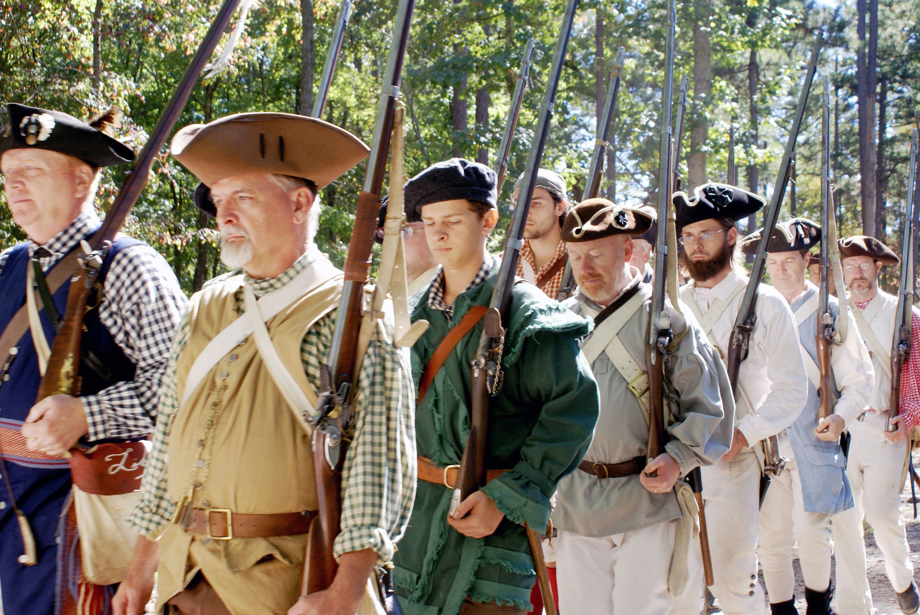 Militia reenactors march with weapons on their shoulders as they prepare to give a firing demonstration.