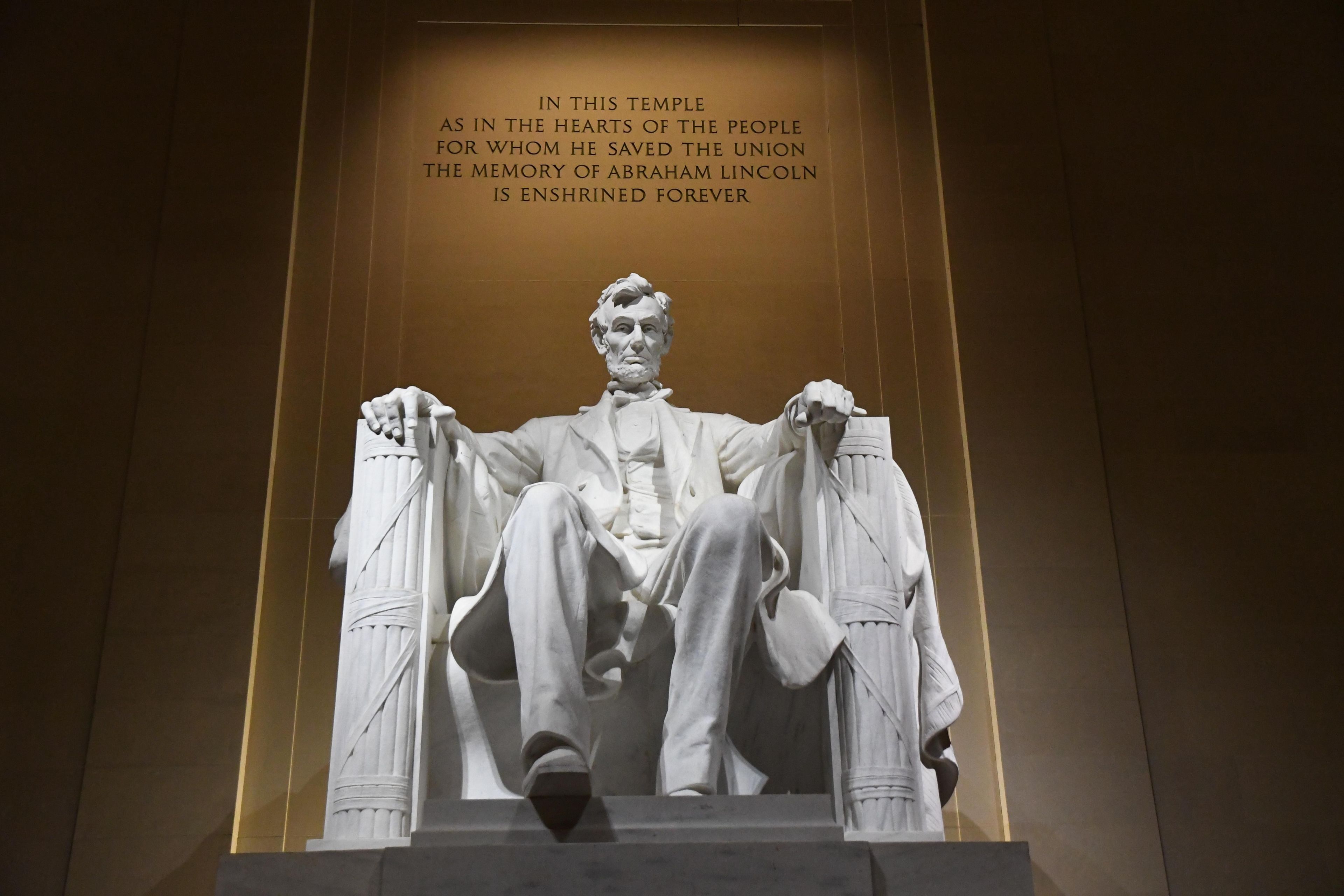 Statue of Abraham Lincoln sitting inside the Lincoln Memorial with a quote above "IN THIS TEMPLE AS IN THE HEARTS OF THE PEOPLE FOR WHOM HE SAVED THE UNION THE MEMORY OF ABRAHAM LINCOLN IS ENSHRINED FOREVER"