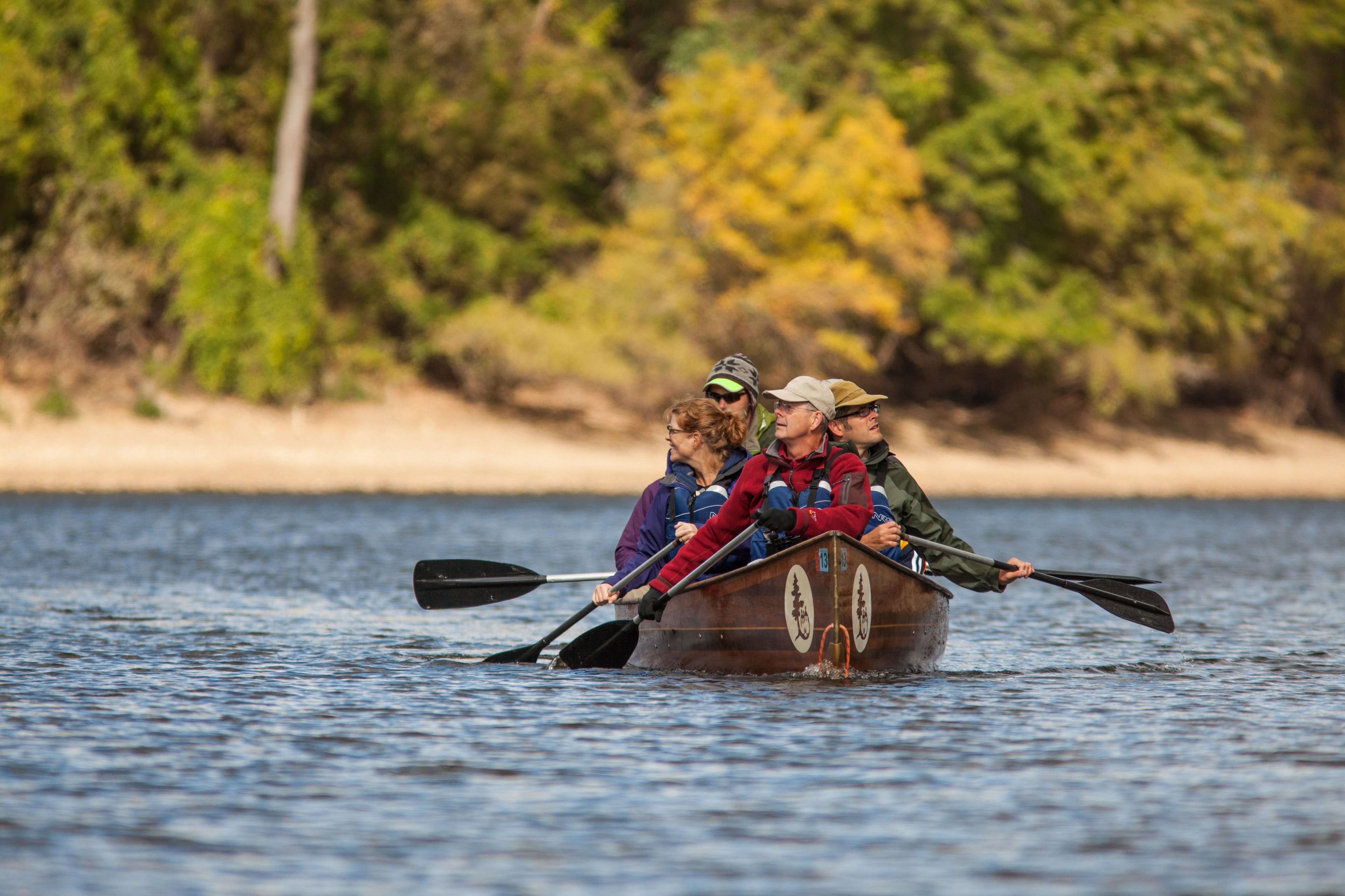 A Voyageur canoe makes headway up a river while surrounded by autumnal color.