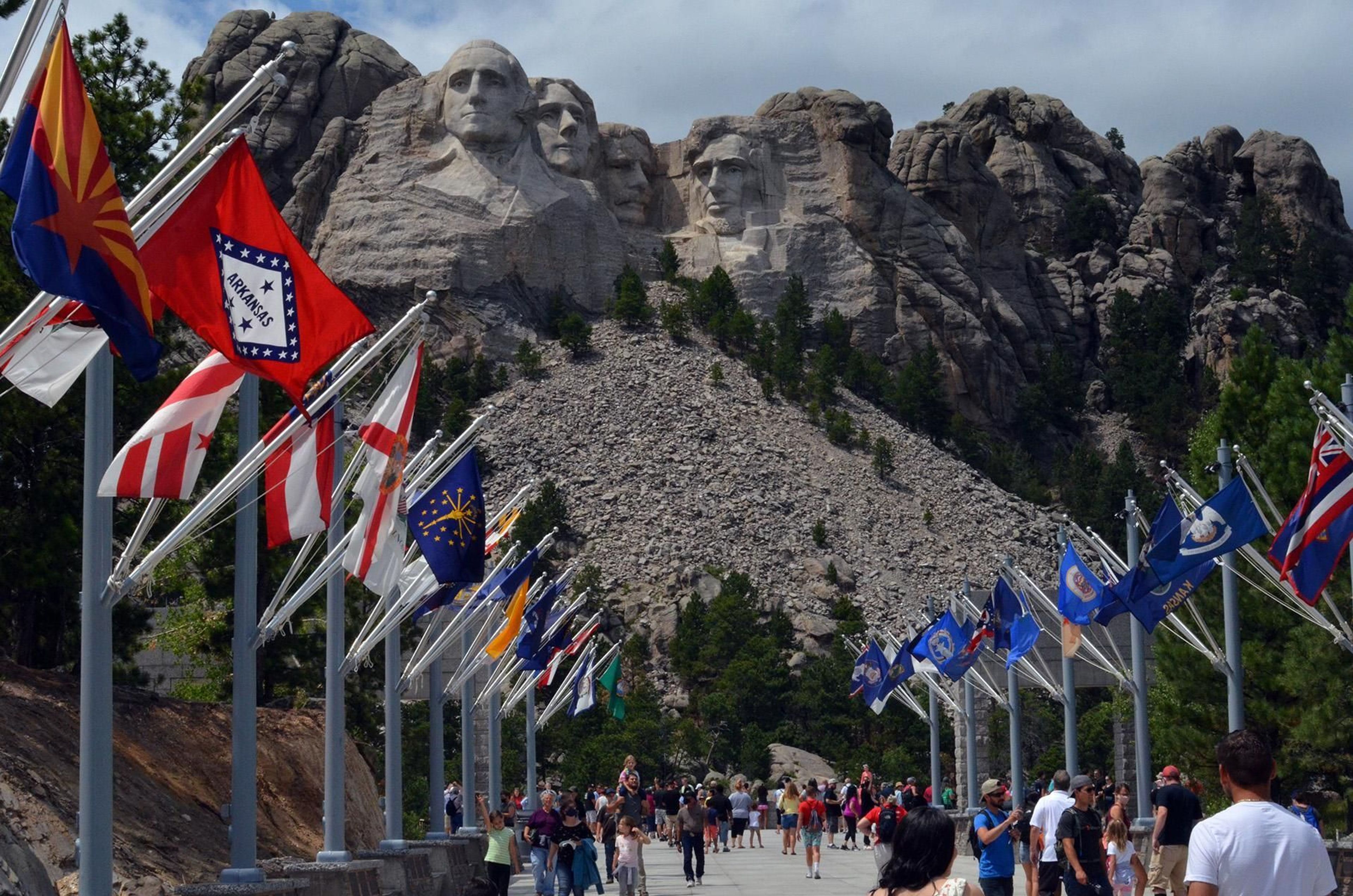 Visitors walking along the Avenue of Flags with Mount Rushmore in the background.