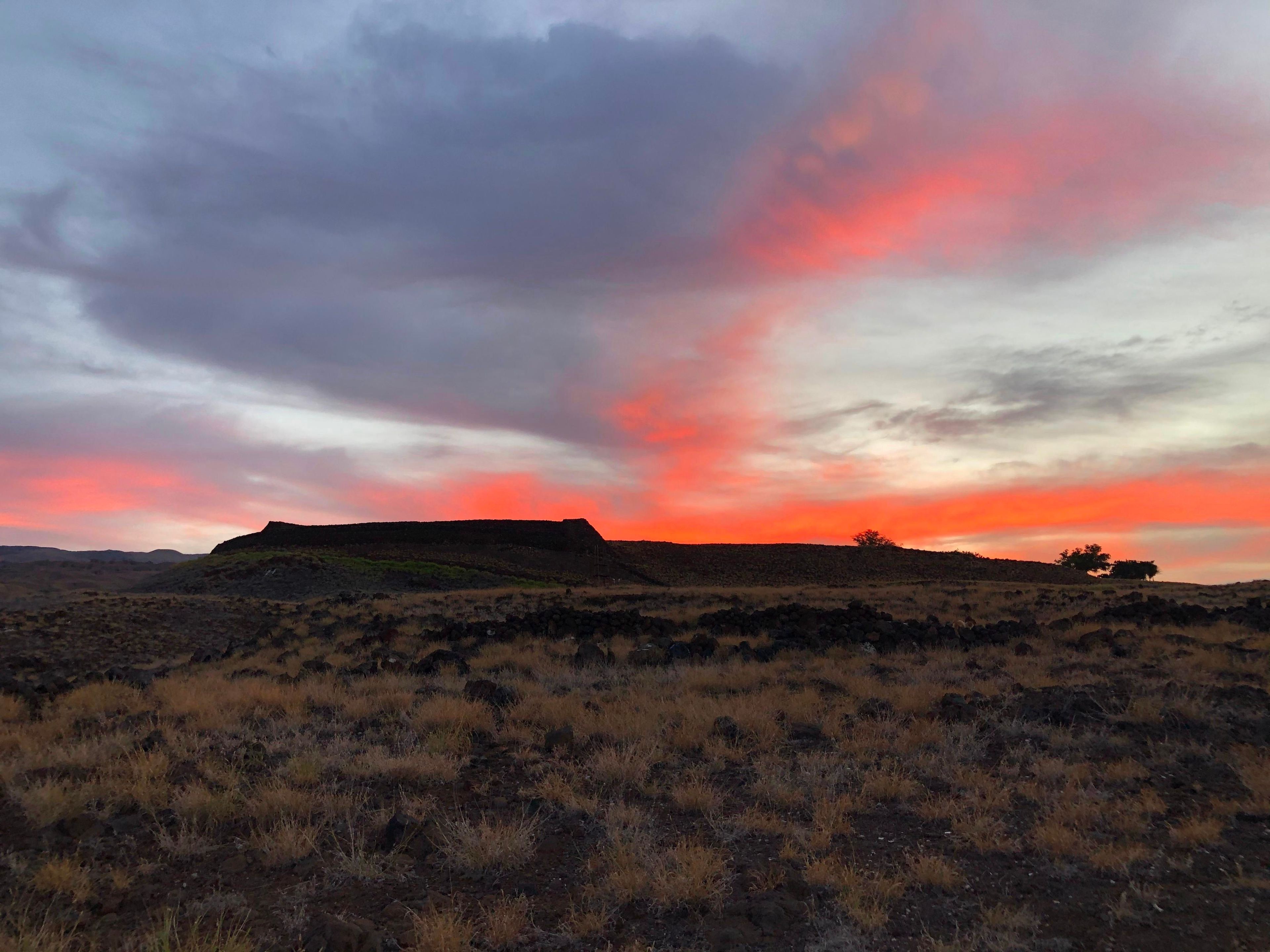 Sunrise with a bright orange red glow rising above Pu'ukoholā Heiau.