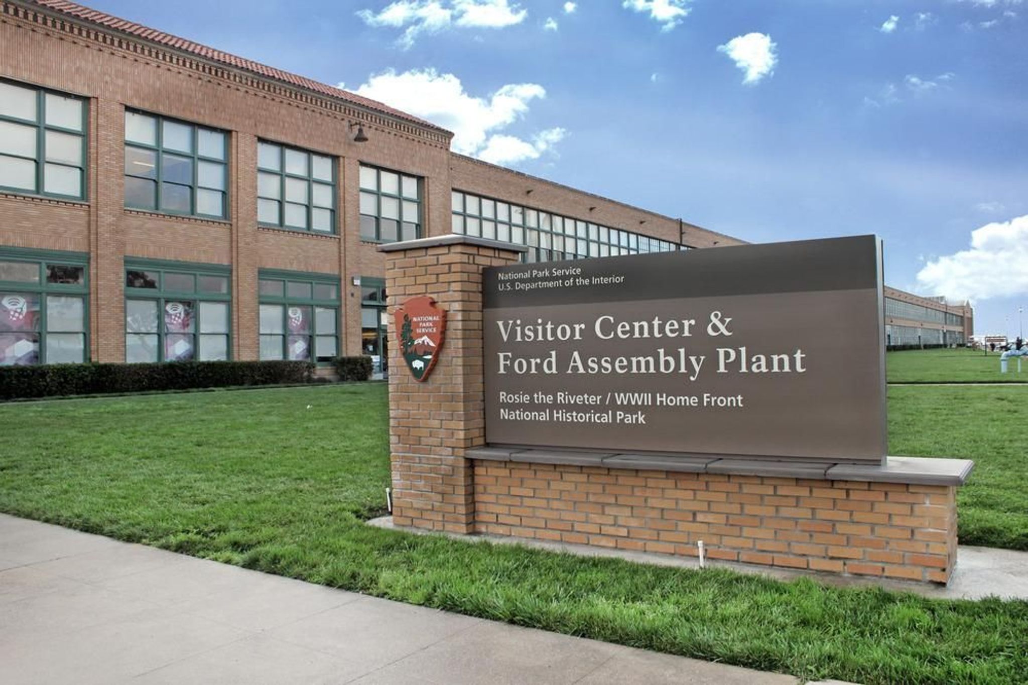 Visitor Center entrance sign with historic Ford Building in the background.