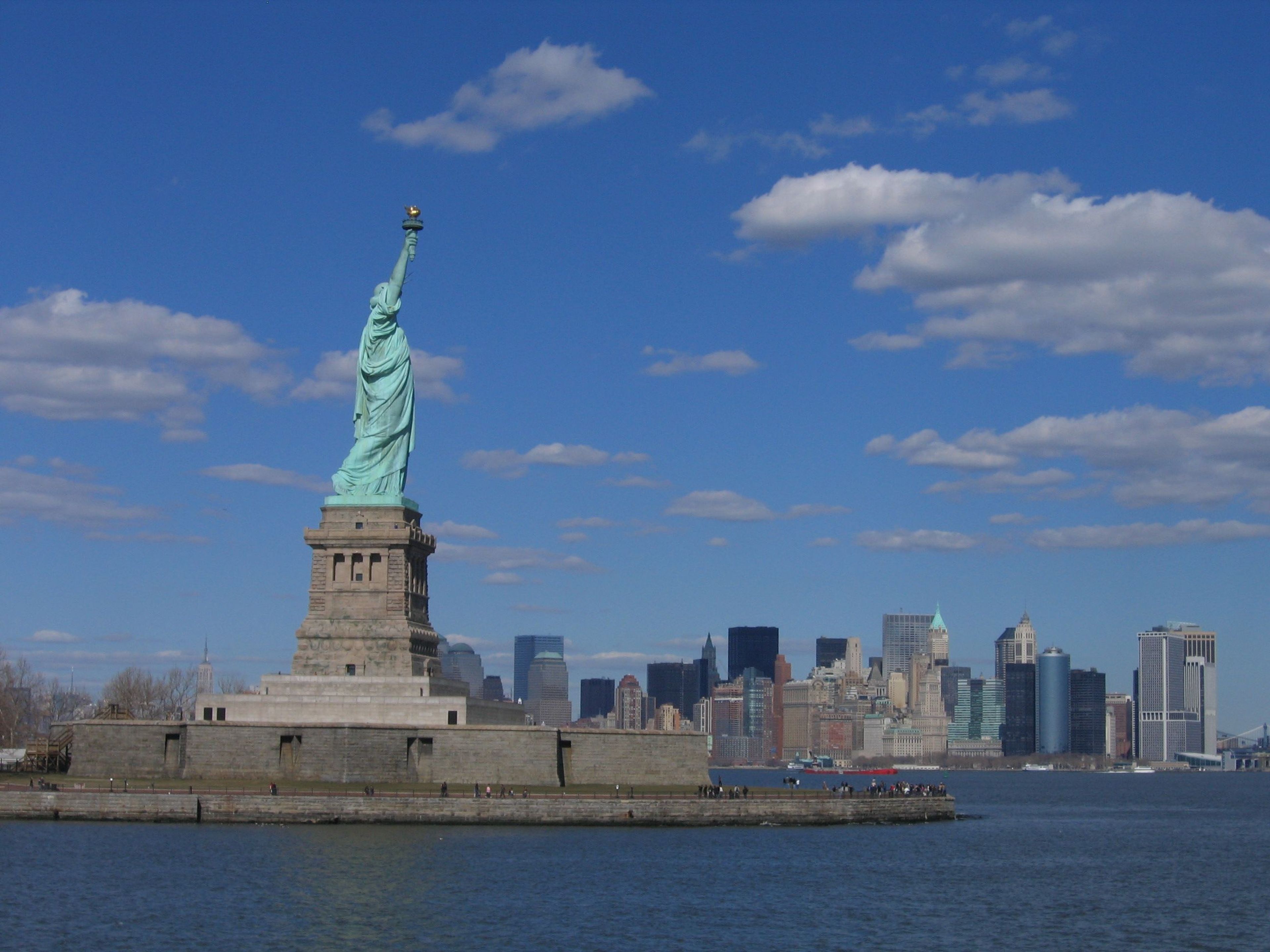 Statue of Liberty stands tall on Liberty Island with the skyline of bustling New York City in view.