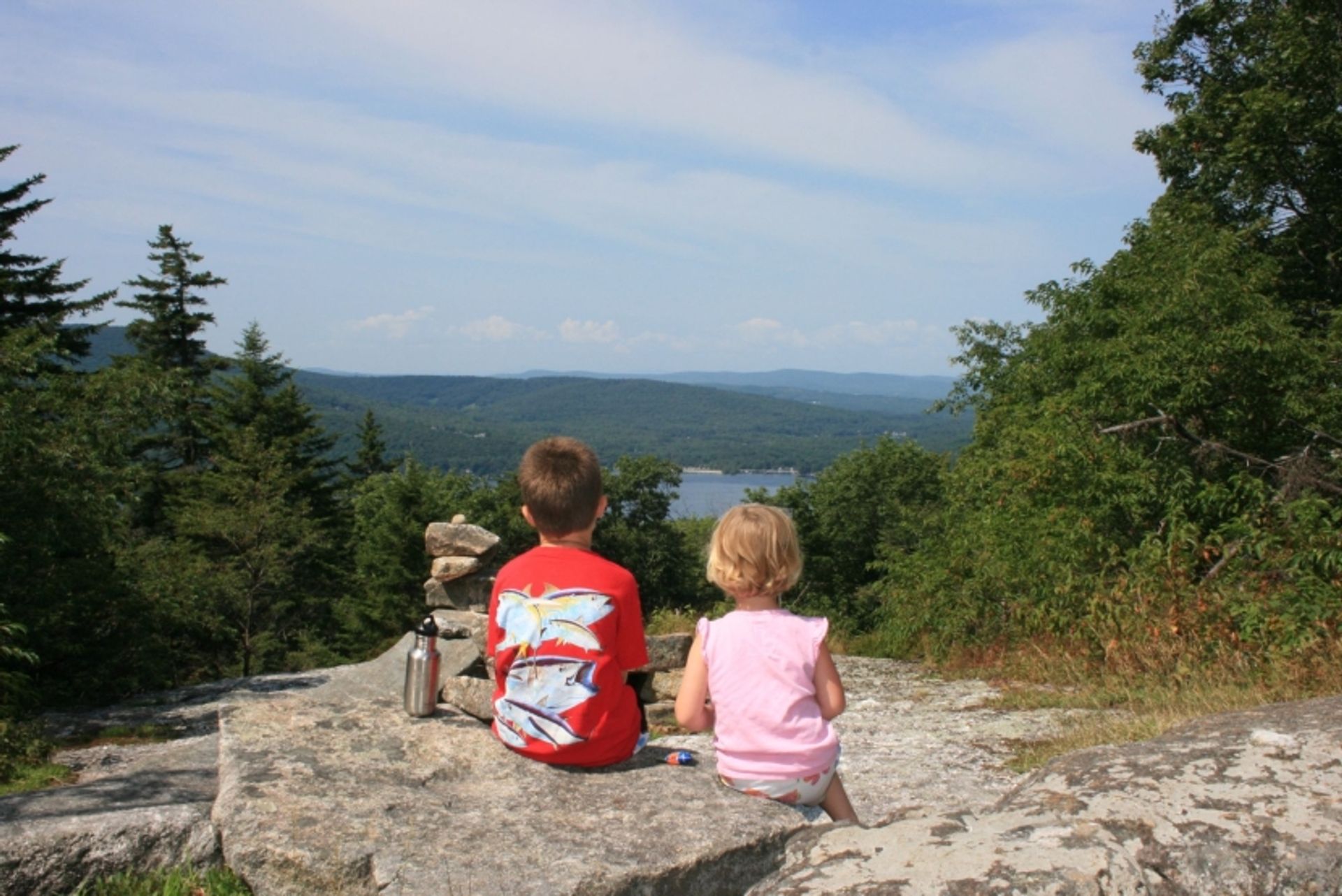 Two children sit facing the view from Summit Hill at Hay Reservation in summer.