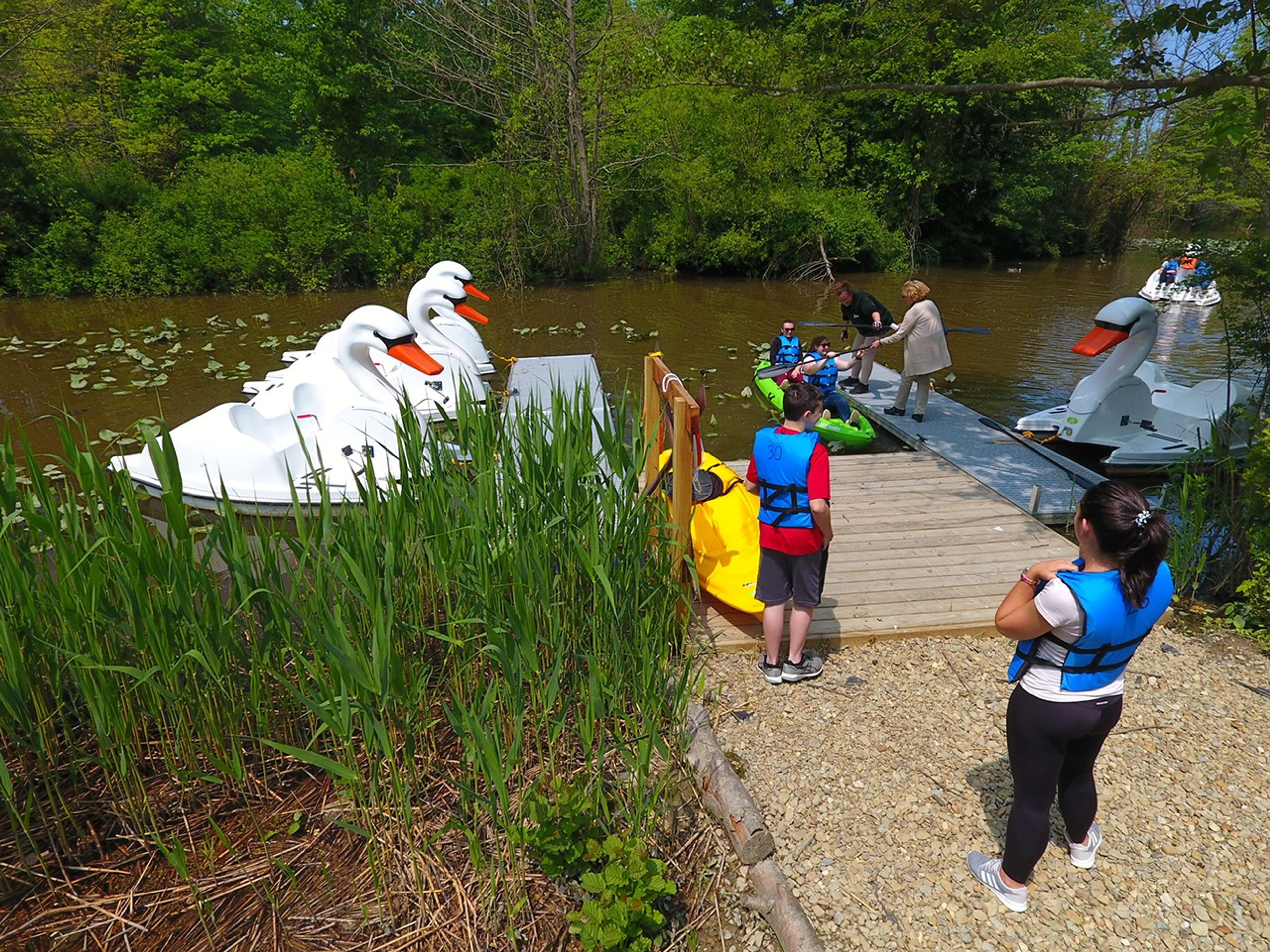 People standing on a dock next to swan boats getting into a kayak at Geneva State Park