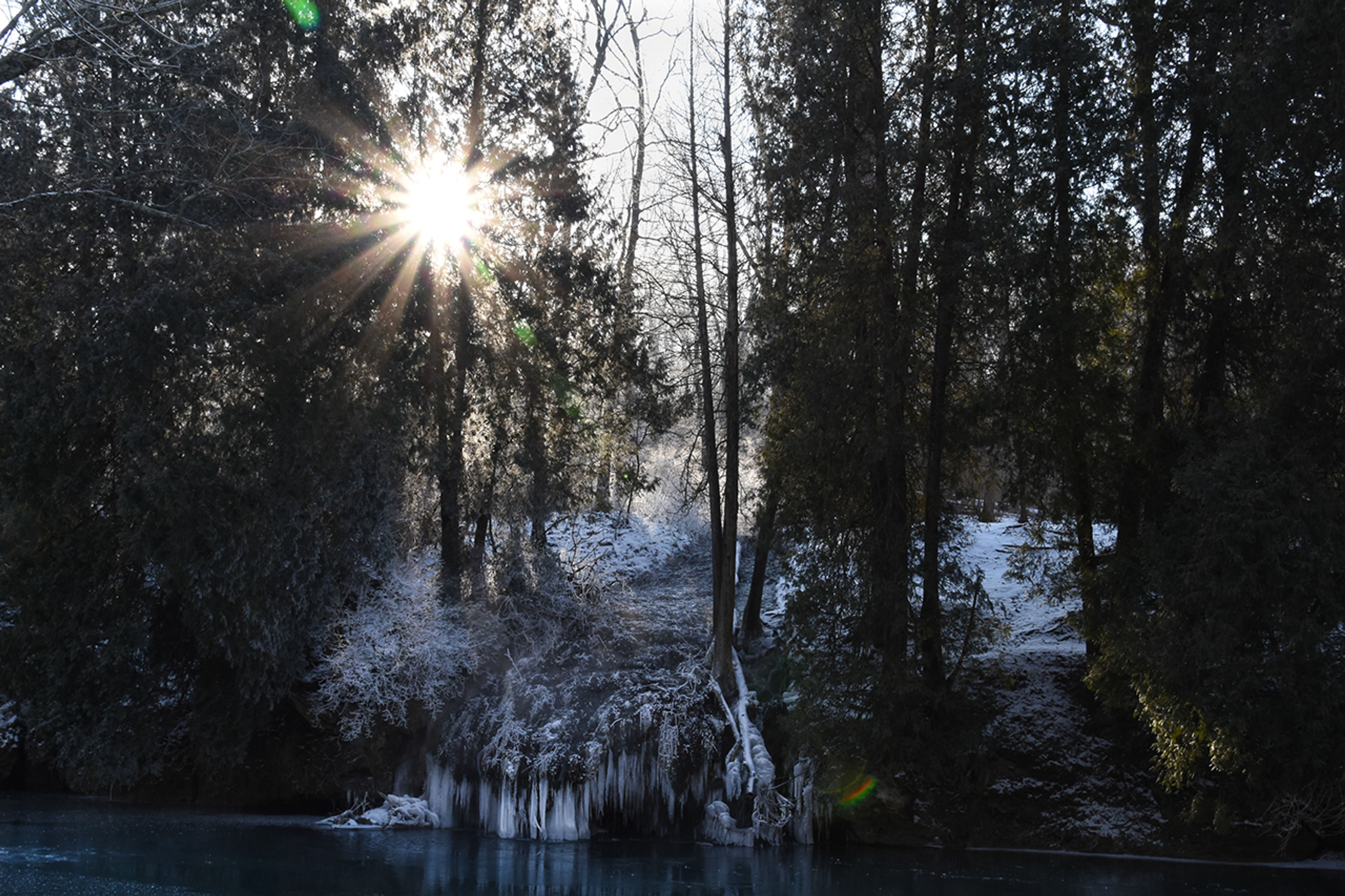 Sun shining through the trees over a frozen waterfall at John Bryan State Park