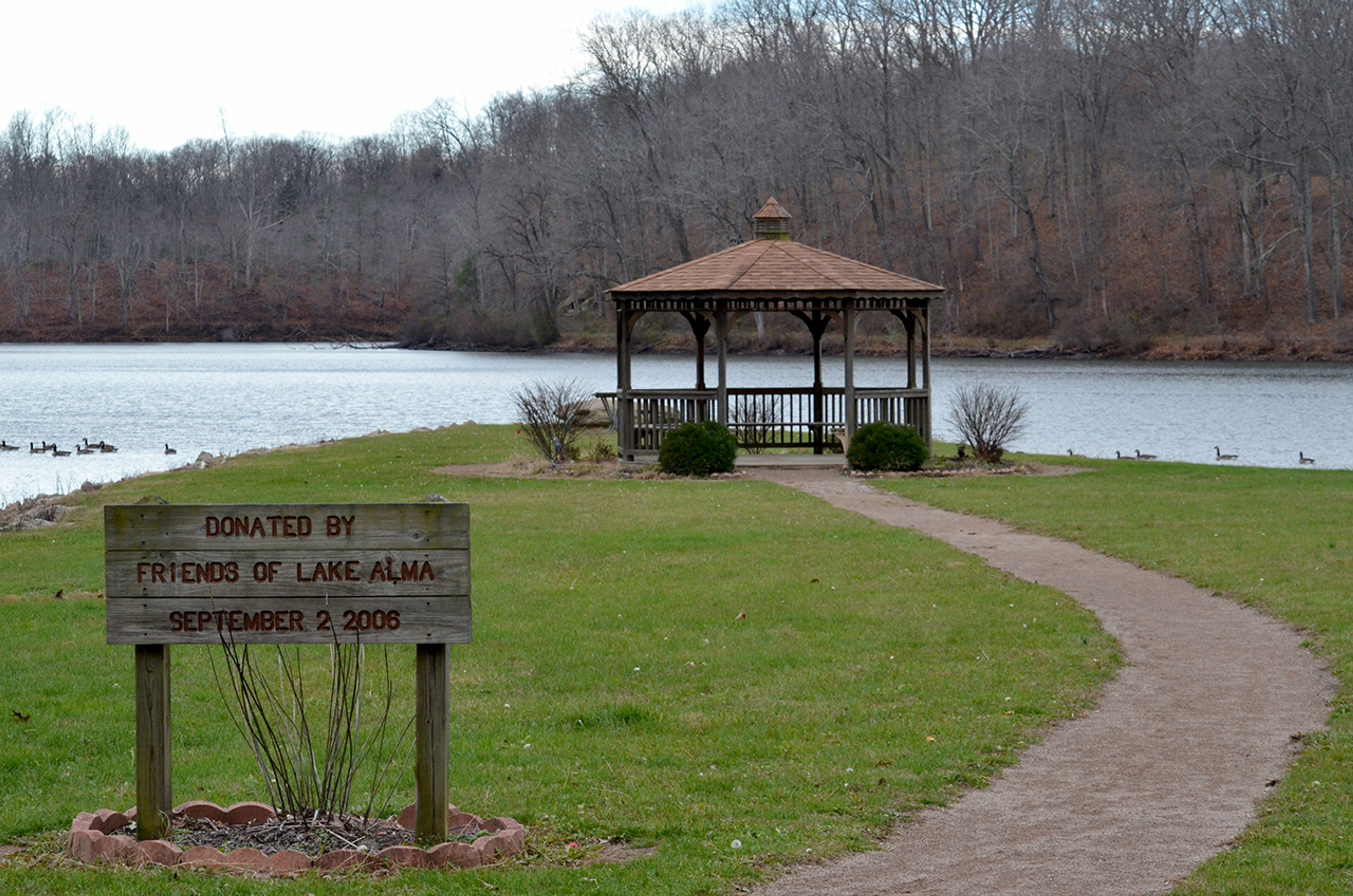 A gazebo next to a lake with a wooden sign in front at Lake Alma State Park