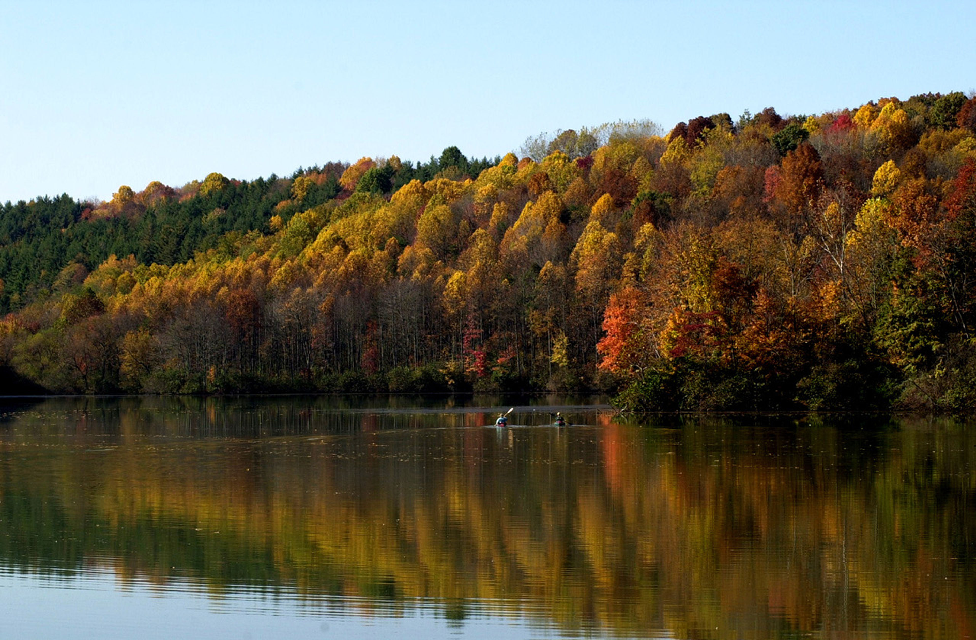 A lake with orange, red, and yellow trees in the background at Lake Logan State Park