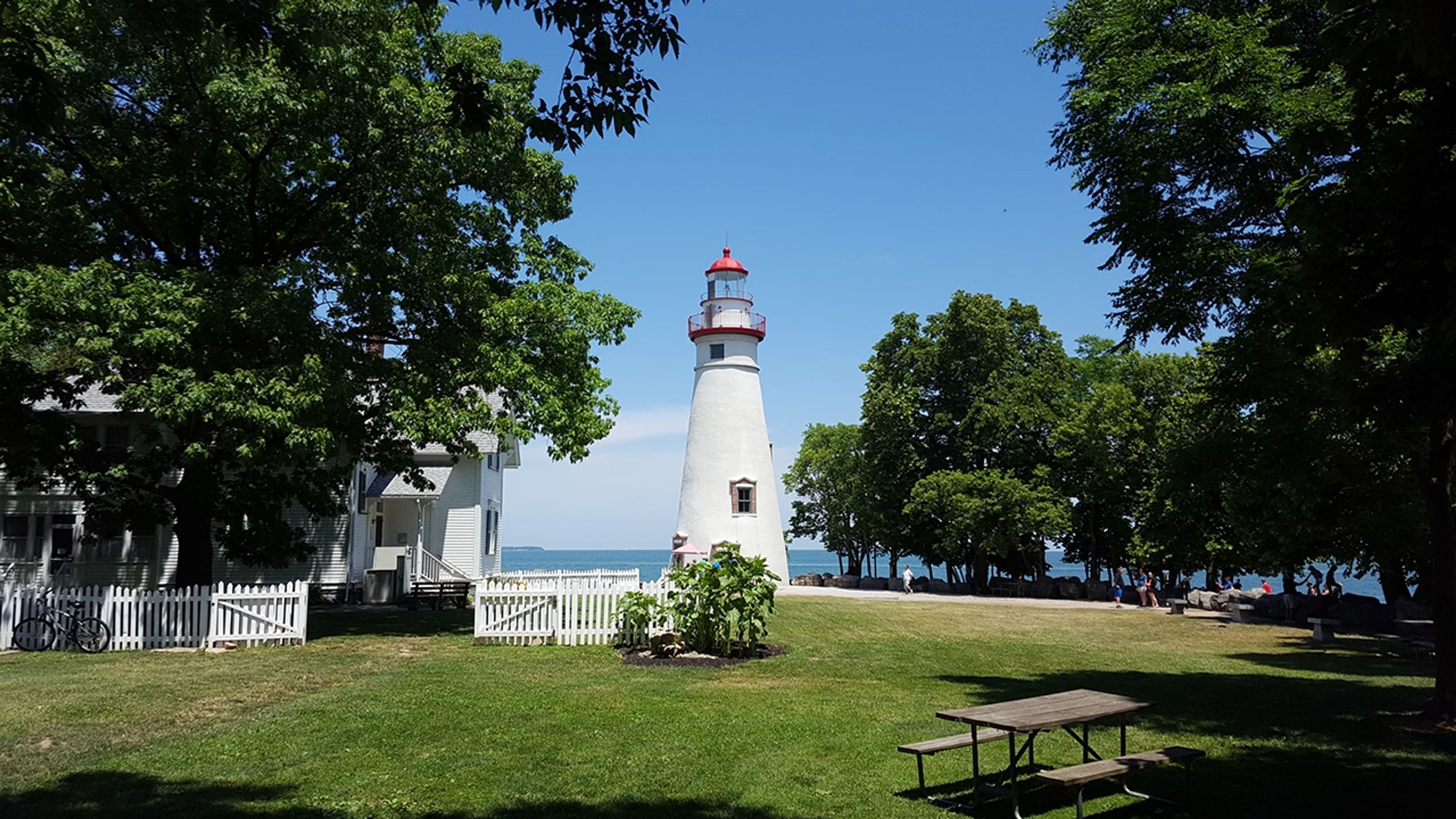 A lighthouse and house with a white fence and trees surrounding at Marblehead Lighthouse State Park