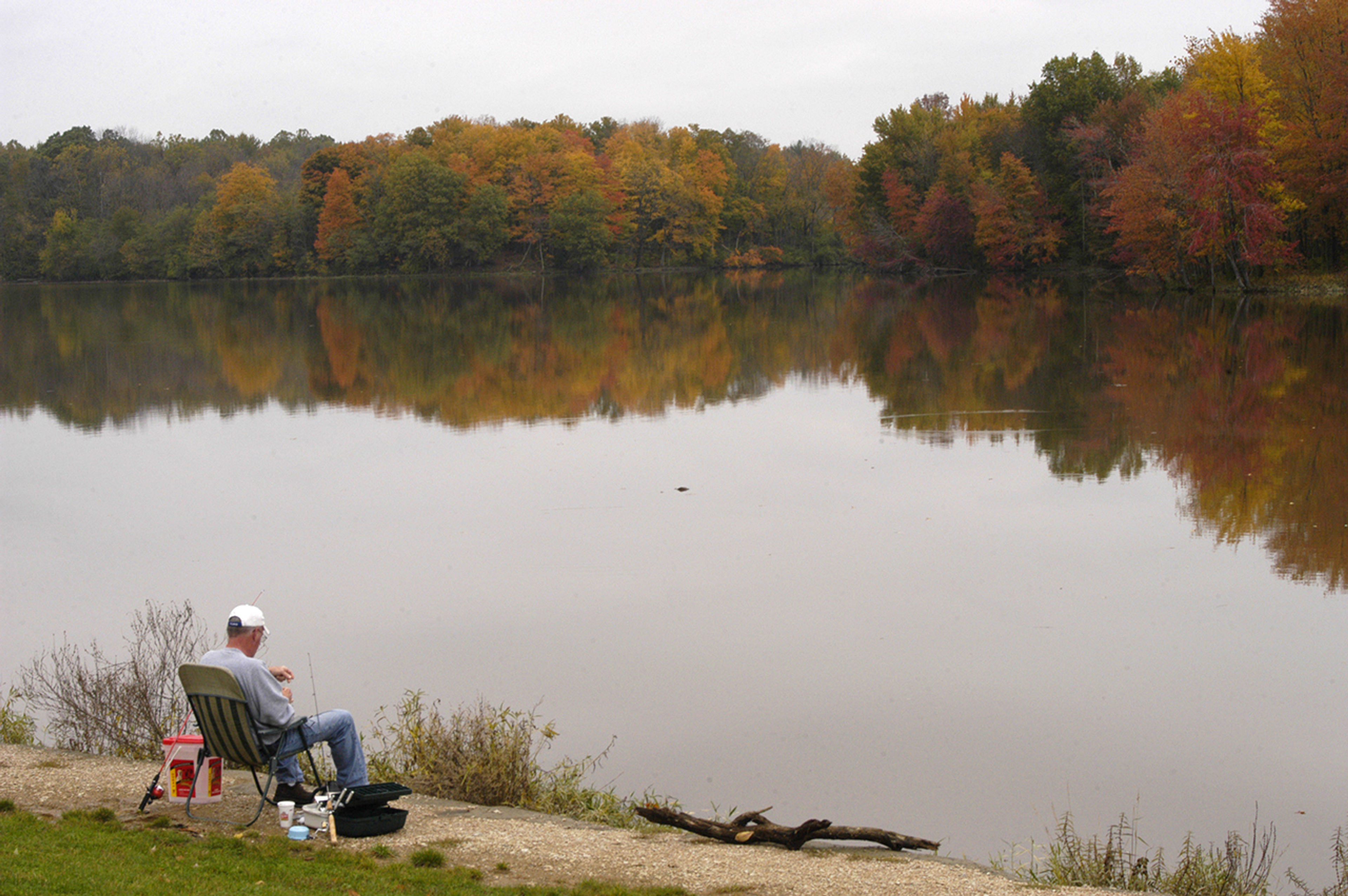 Person sitting by a body of water fishing at Stonelick State Park