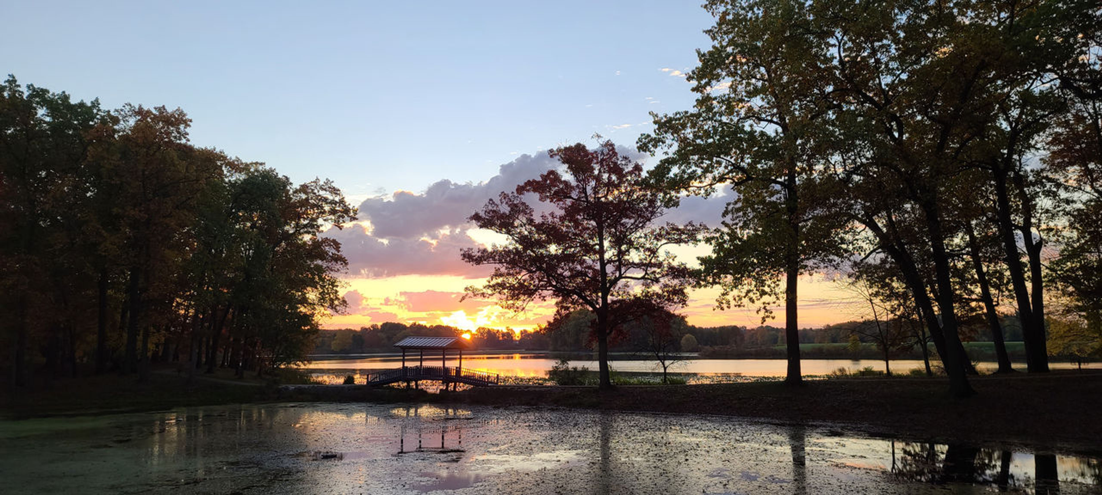 A sunrise over a body of water with a small bridge and trees at Wingfoot Lake State Park