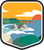 An illustrated badge for the Guam community depicting a tropical beach with blue water and rock formations under a sunny sky.