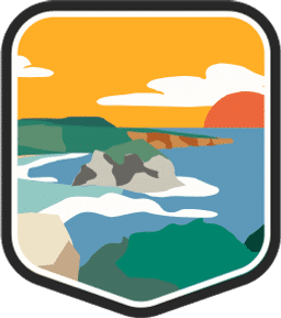 An illustrated badge for the Guam community depicting a tropical beach with blue water and rock formations under a sunny sky.