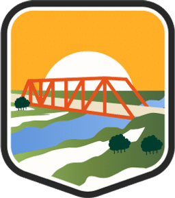 An illustrated badge for the Iowa community of a bridge over a river running through green fields under a blue sky.