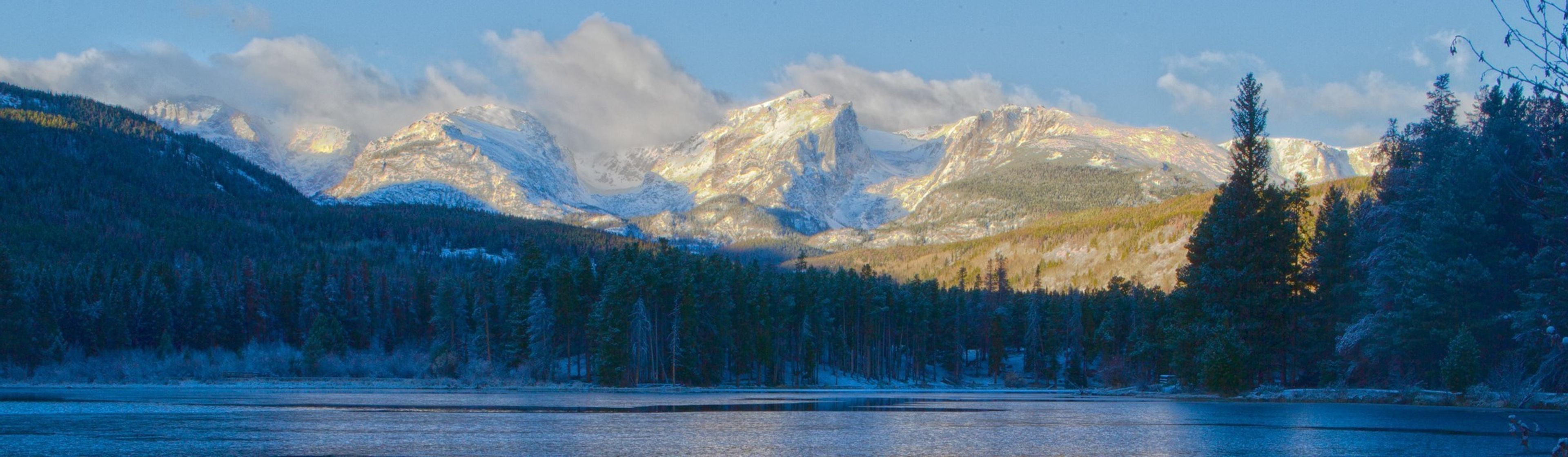 Partially iced-over Sprague Lake with the snowy peaks of the Continental Divide in the background.