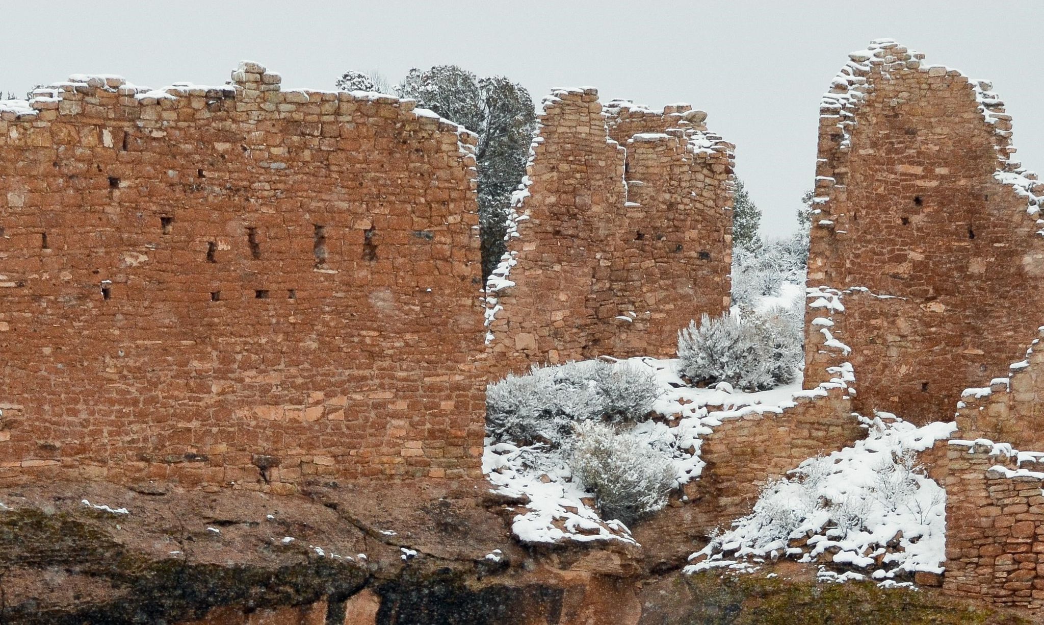Stone structures blanketed with snow sit on the rim of a canyon at Hovenweep National Monument.