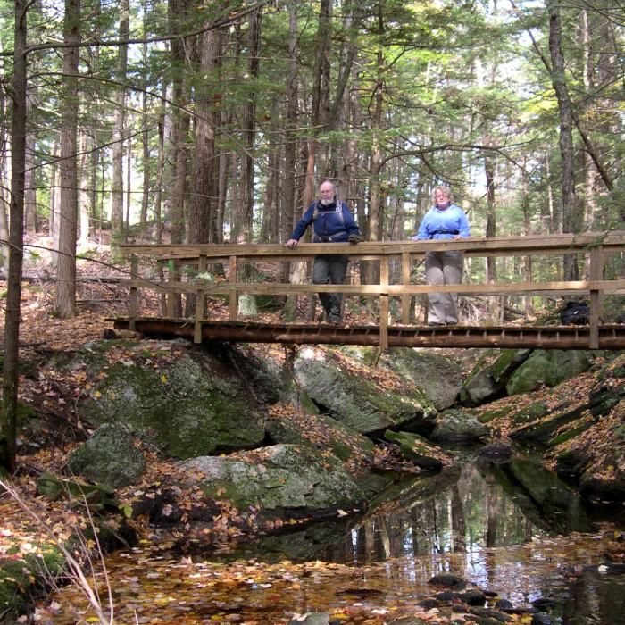 Two hikers stand on a bridge over boulders and water at the reservation.