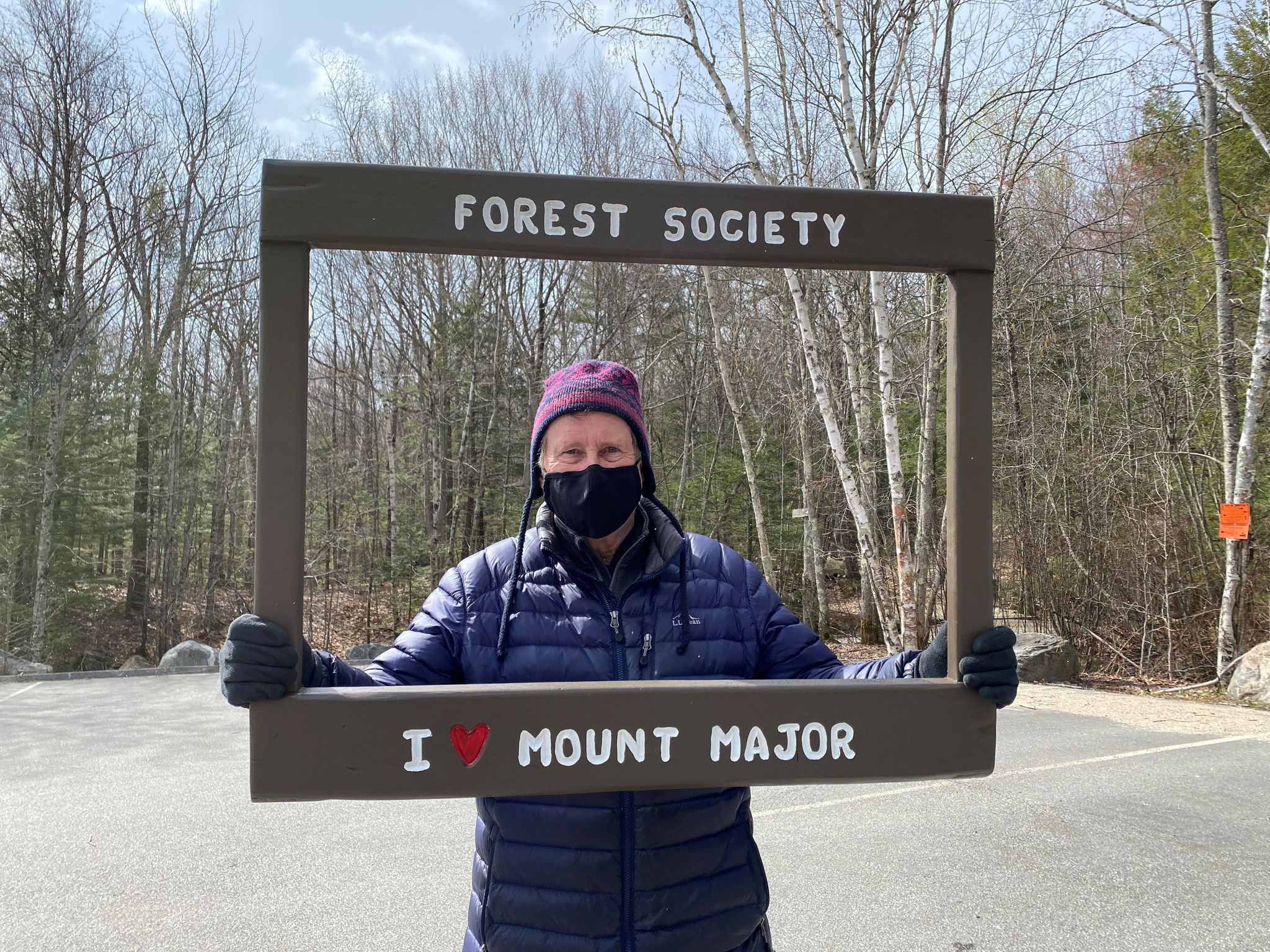 A man holds a sign that says "I [heart] Mount Major," at the trailhead in winter.