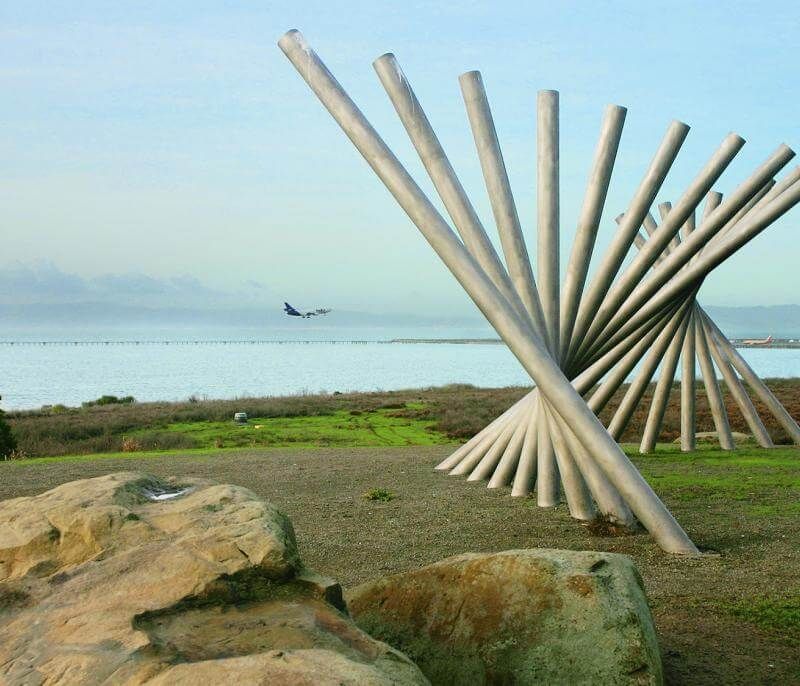 View along water of plane landing and cool wooden spiral art installation.