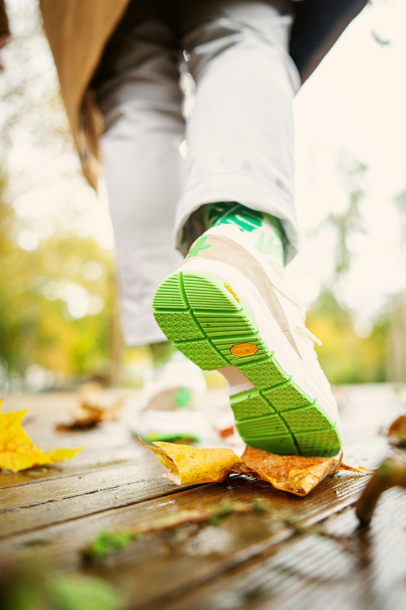 White shoe with green sole walking on a wet, wooden bridge, with fall leaves