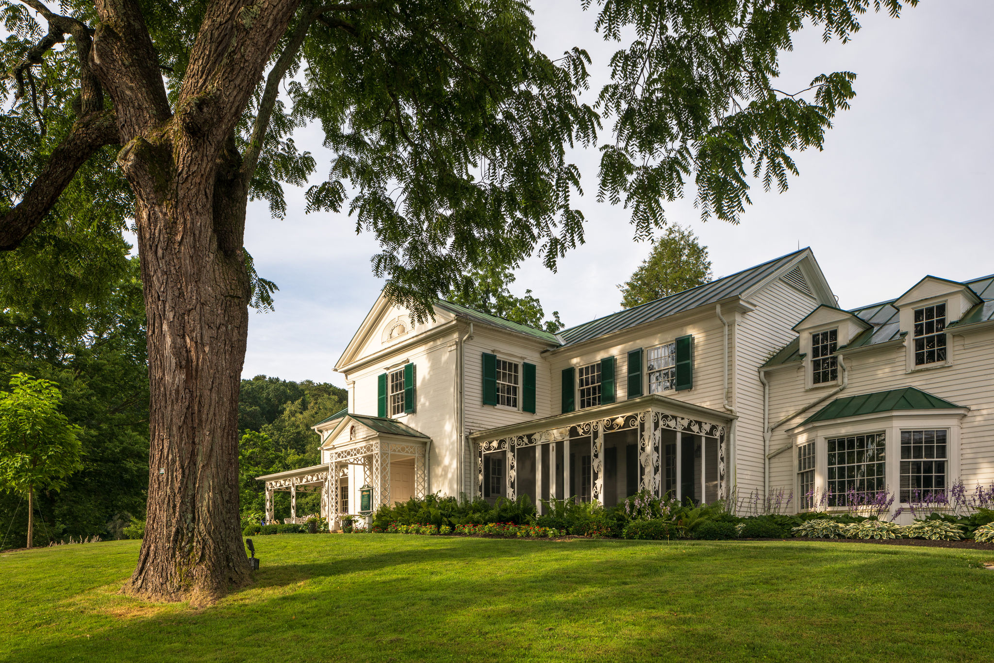 a view of the white malabar farm house with green accents on the hill with a tree to the right of it