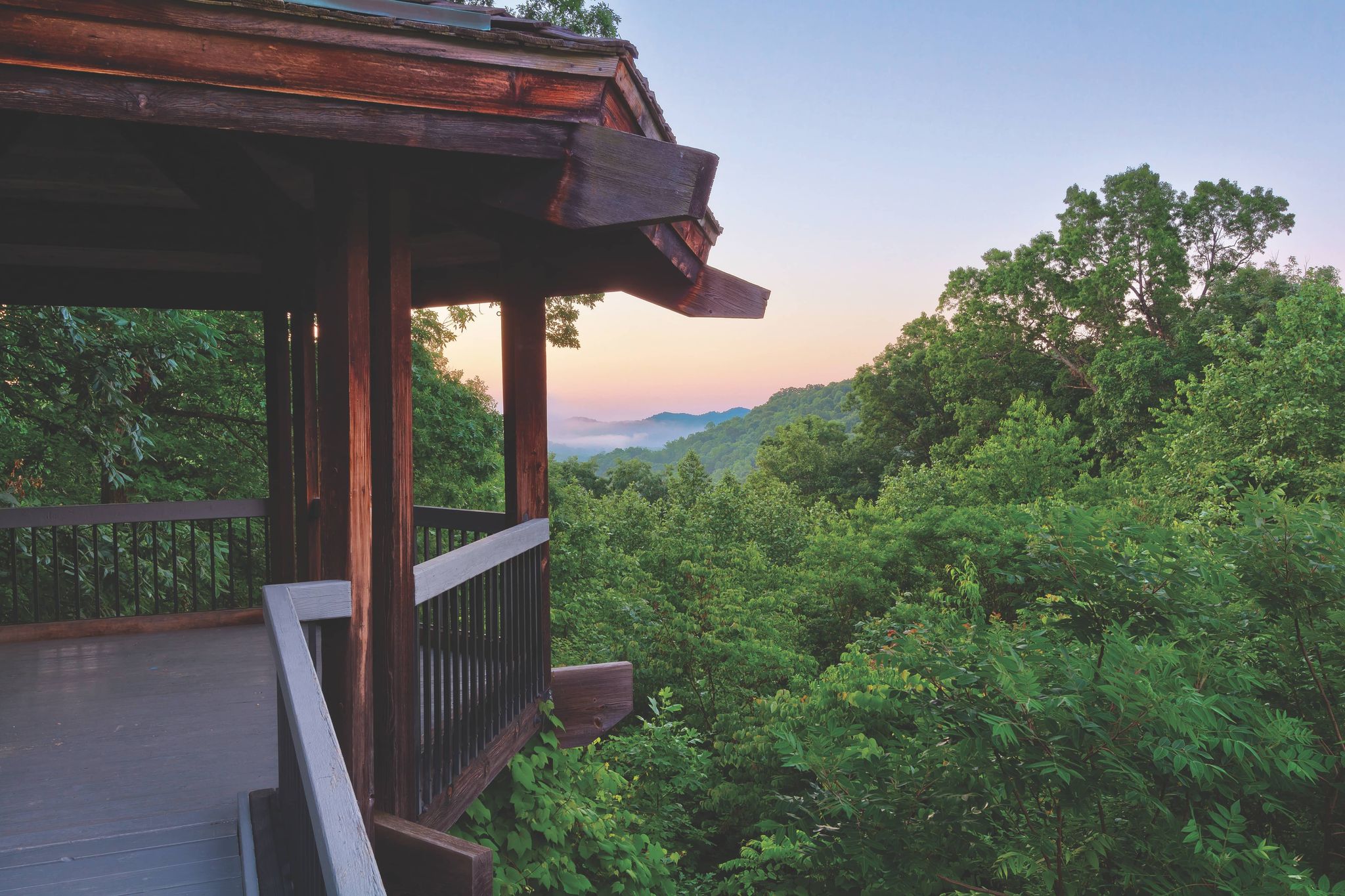 view from a cabin balcony looking at the sunset and green trees in the distance at shawnee state park