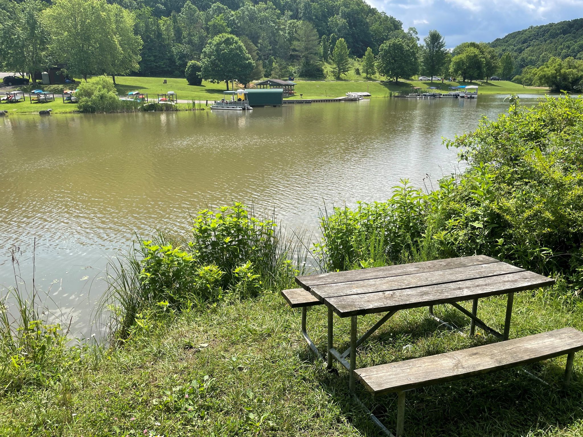 picnic table sitting in front of a table in front of strouds run lake with full green trees surrounding